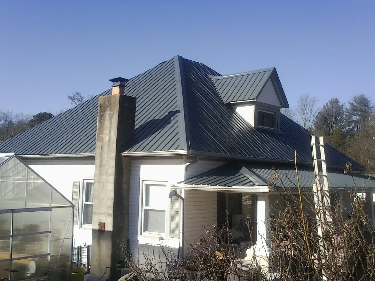 Dark blue standing seam metal roof on a white farmhouse with dormer — Slate & Tile Roof Repair by Roofing Brothers in Austin