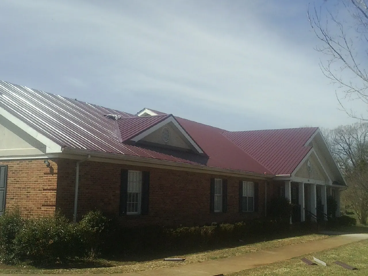 Red metal roof with gabled entries on a long brick building, from a Hail Damage Roof Repair job in Austin