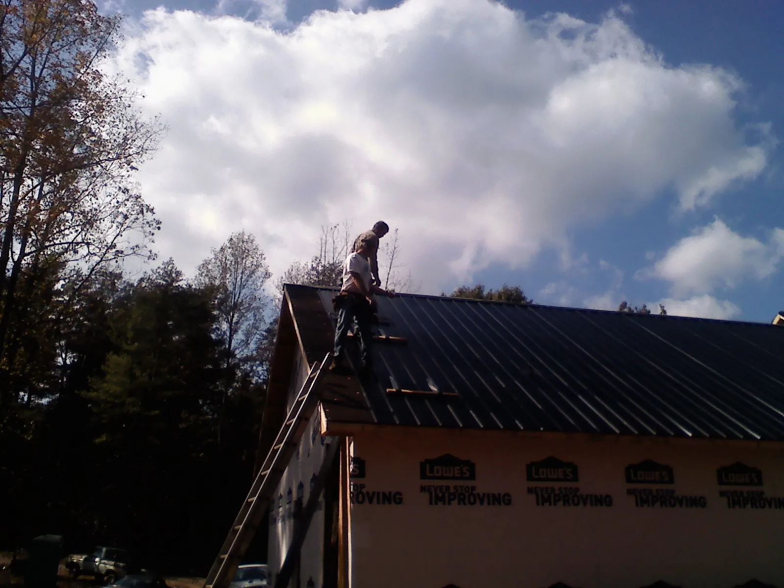 Roofer fastening dark metal panels high against a cloudy sky, from a Roof Inspection job in Austin
